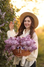 Photo of Smiling woman with basket of lilac flowers outdoors in morning