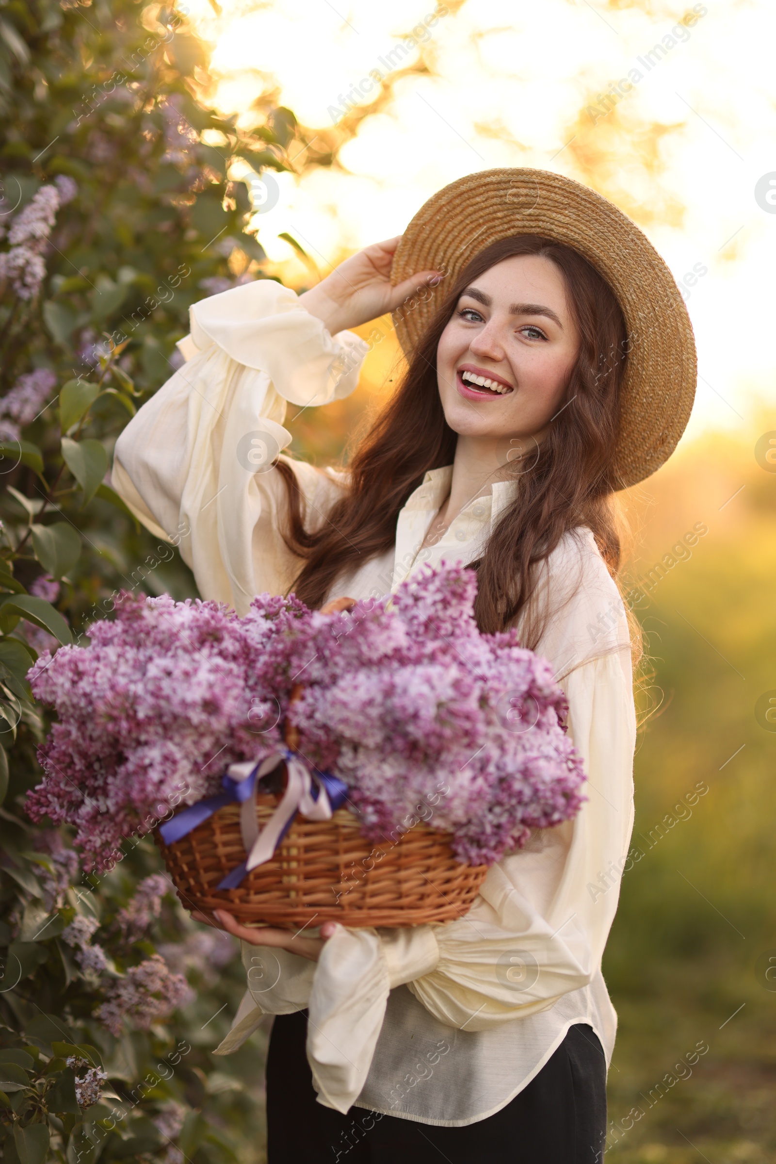 Smiling woman with basket of lilac flowers outdoors in morning Photo of Smiling woman with basket of lilac flowers outdoors in morning