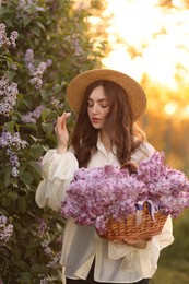 Photo of Beautiful woman with basket of lilac flowers outdoors in morning