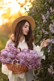 Photo of Beautiful woman with basket of lilac flowers outdoors in morning