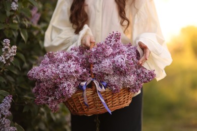 Photo of Woman with basket of lilac flowers in morning, closeup