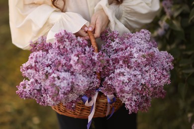 Photo of Woman with basket of lilac flowers outdoors, closeup