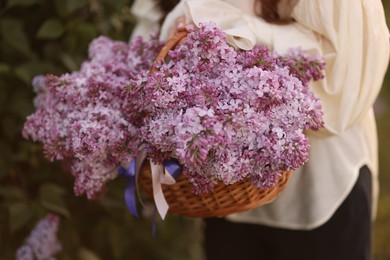 Photo of Woman with basket of lilac flowers outdoors, closeup