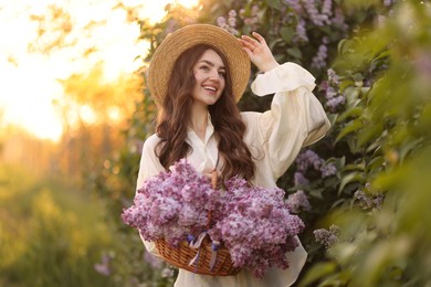 Photo of Smiling woman with basket of lilac flowers near bush outdoors in morning