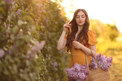 Photo of Beautiful woman with bag of lilac flowers near bush outdoors in morning