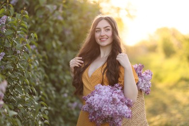 Photo of Smiling woman with bag of lilac flowers near bush outdoors in morning