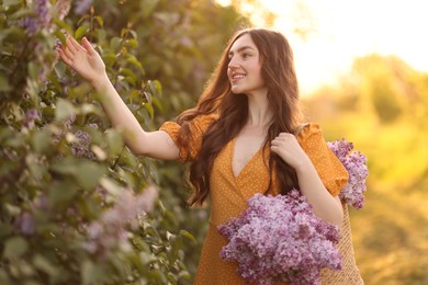 Photo of Smiling woman with bag of lilac flowers near bush outdoors in morning
