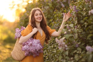 Photo of Smiling woman with bag of lilac flowers near bush outdoors in morning