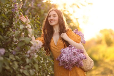 Photo of Smiling woman with bag of lilac flowers near bush outdoors in morning