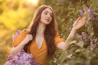 Photo of Beautiful woman with bag of lilac flowers near bush outdoors in morning