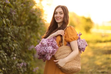 Photo of Smiling woman with bag of lilac flowers near bush outdoors in morning