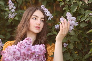 Photo of Beautiful woman with lilac flowers near bush outdoors