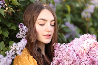 Photo of Beautiful woman with lilac flowers near bush outdoors