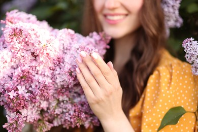 Photo of Smiling woman with bouquet of lilac flowers outdoors, selective focus