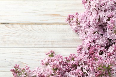Photo of Beautiful lilac flowers on light wooden table, closeup. Space for text