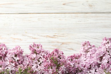 Photo of Beautiful lilac flowers on light wooden table, closeup. Space for text