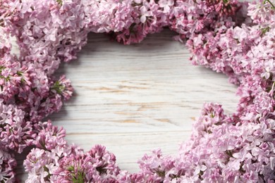 Photo of Frame of beautiful lilac flowers on light wooden table, above view. Space for text