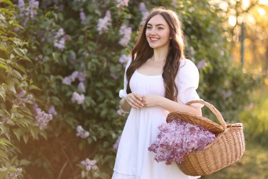 Photo of Smiling woman with basket of lilac flowers near bush in morning