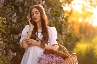 Photo of Beautiful woman with basket of lilac flowers outdoors in morning