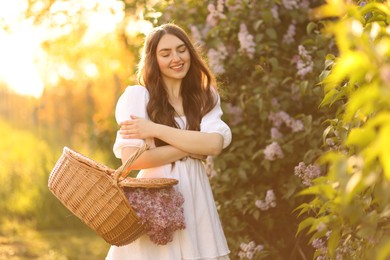 Photo of Smiling woman with basket of lilac flowers outdoors in morning