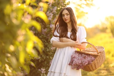 Photo of Beautiful woman with basket of lilac flowers outdoors in morning