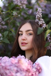 Photo of Beautiful woman among lilac flowers and leaves outdoors, closeup