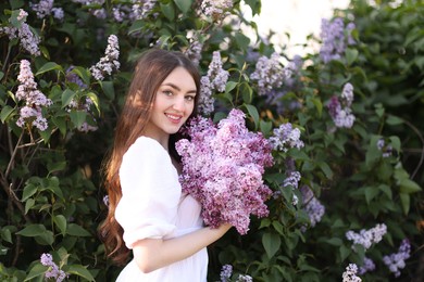 Photo of Smiling woman among lilac flowers and leaves outdoors
