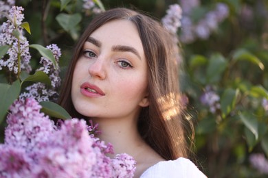 Photo of Beautiful woman among lilac flowers and leaves outdoors, closeup