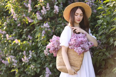 Photo of Beautiful woman with bag of lilac flowers near bush outdoors