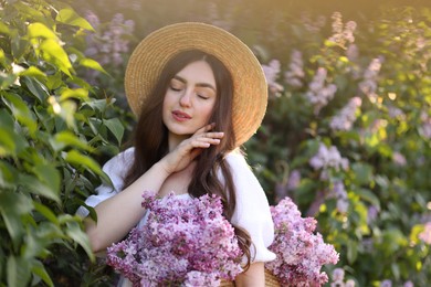 Photo of Beautiful woman with bag of lilac flowers near bush outdoors in morning