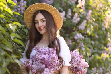 Photo of Smiling woman with bag of lilac flowers near bush outdoors