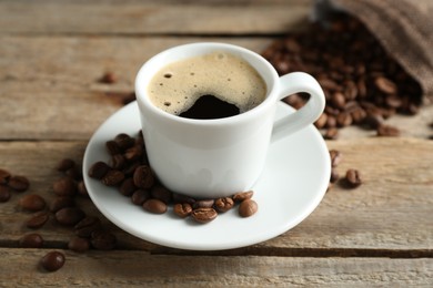 Photo of Aromatic coffee in cup and beans on wooden table, closeup