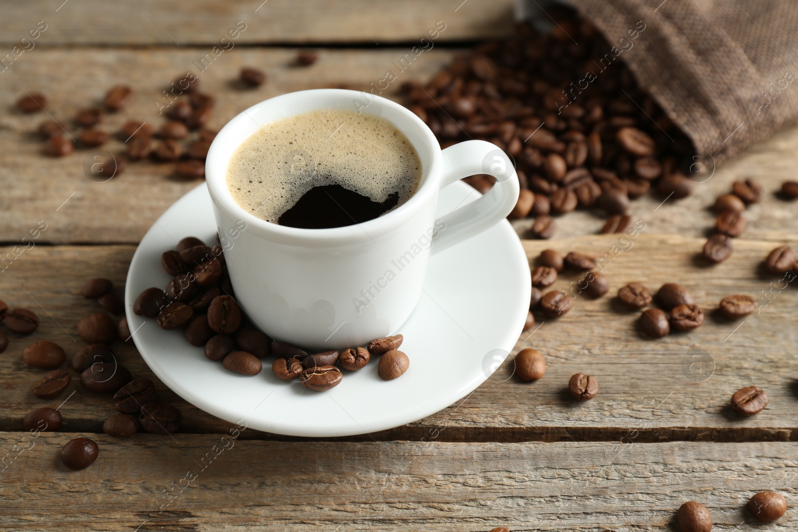 Aromatic coffee in cup and beans on wooden table, closeup Photo of Aromatic coffee in cup and beans on wooden table, closeup