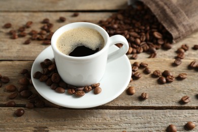 Photo of Aromatic coffee in cup and beans on wooden table, closeup