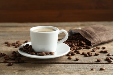 Photo of Aromatic coffee in cup and beans on wooden table, closeup