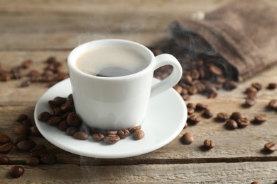 Photo of Aromatic coffee in cup and beans on wooden table, closeup