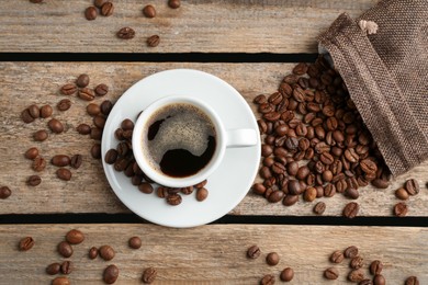 Photo of Aromatic coffee in cup and beans on wooden table, flat lay