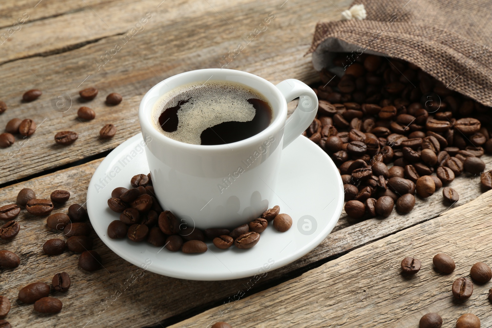 Aromatic coffee in cup and beans on wooden table, closeup Photo of Aromatic coffee in cup and beans on wooden table, closeup