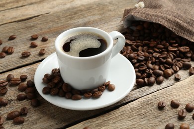 Photo of Aromatic coffee in cup and beans on wooden table, closeup