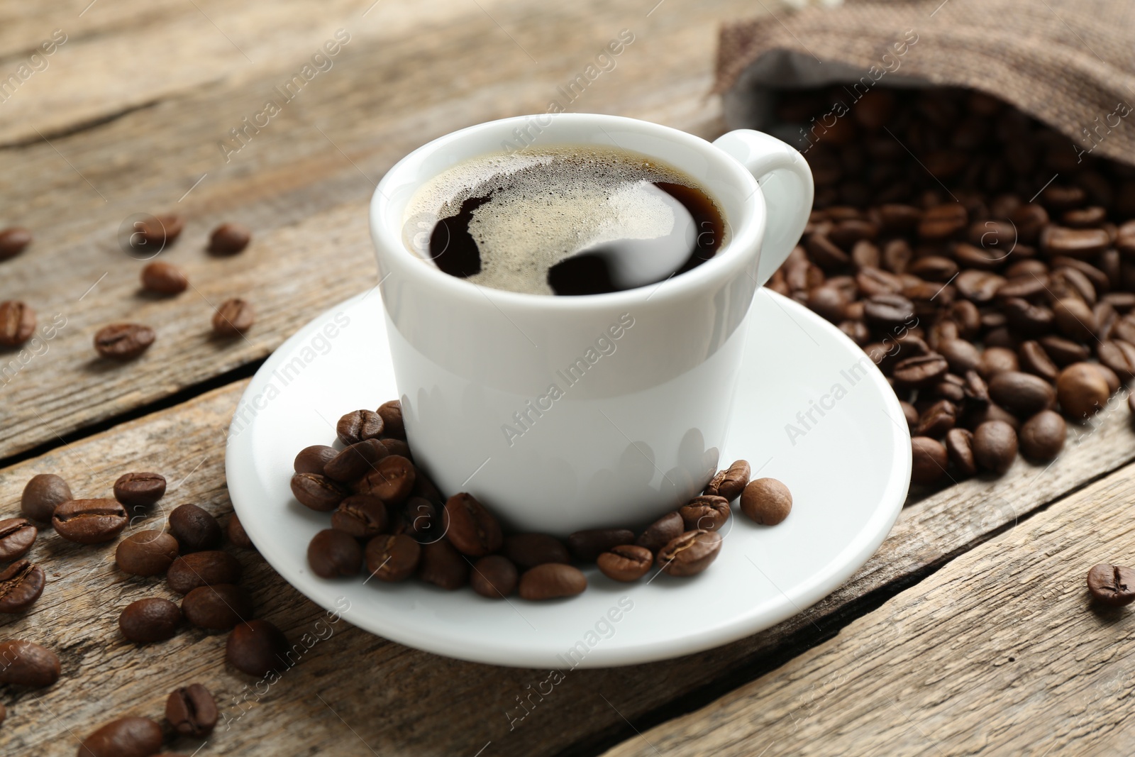 Aromatic coffee in cup and beans on wooden table, closeup Photo of Aromatic coffee in cup and beans on wooden table, closeup
