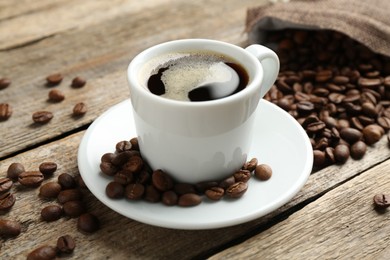 Photo of Aromatic coffee in cup and beans on wooden table, closeup