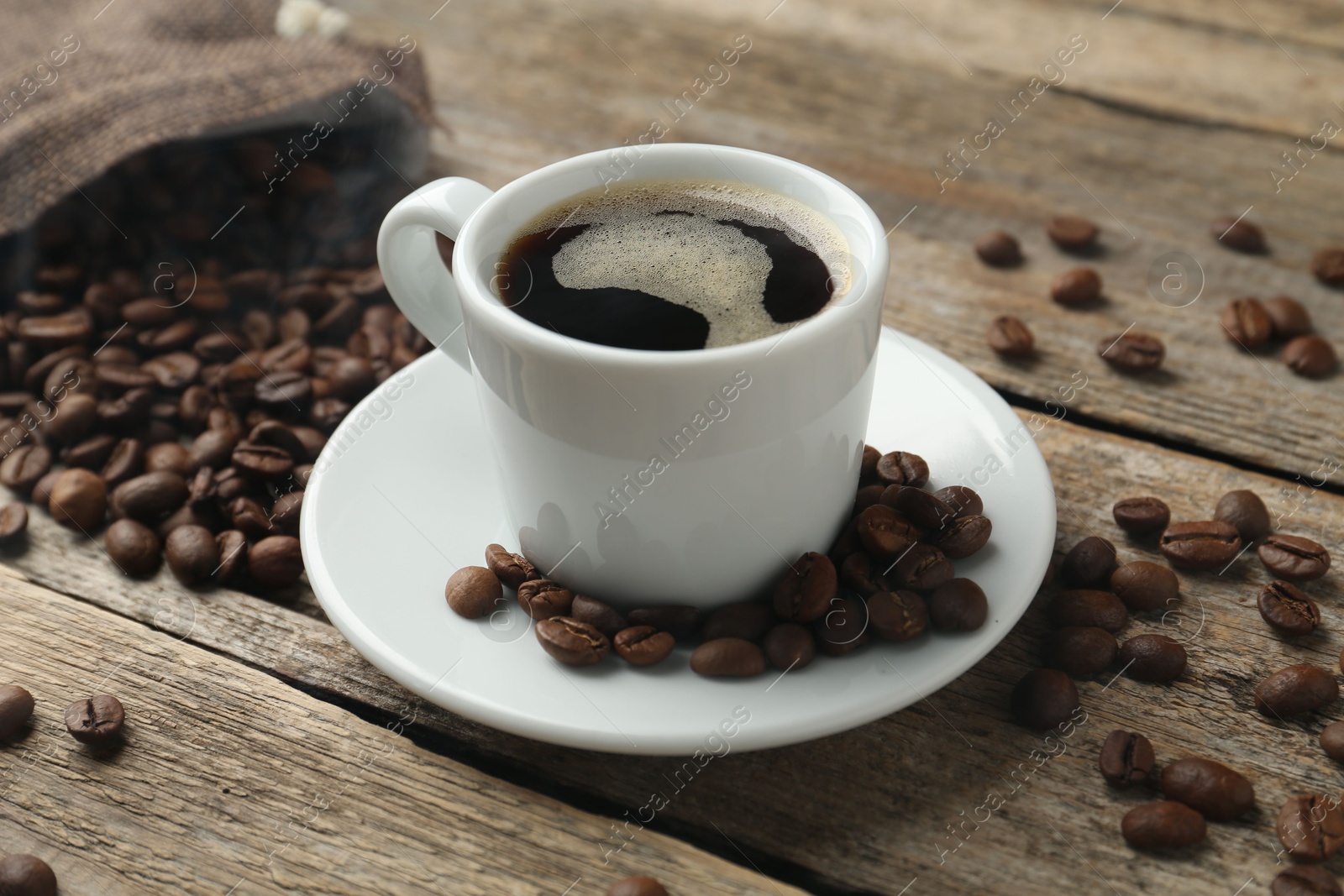 Aromatic coffee in cup and beans on wooden table, closeup Photo of Aromatic coffee in cup and beans on wooden table, closeup