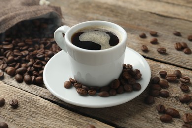Photo of Aromatic coffee in cup and beans on wooden table, closeup
