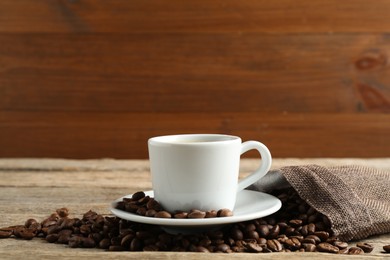 Photo of Aromatic coffee in cup and beans on wooden table