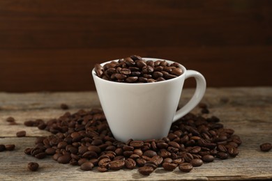 Photo of Aromatic coffee beans and cup on wooden table, closeup