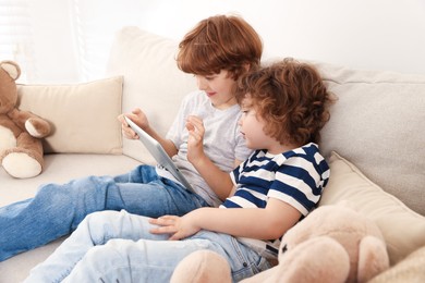 Photo of Cute little brothers with tablet on sofa at home