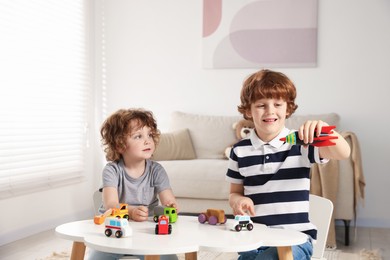 Photo of Cute little brothers playing with toys at table indoors