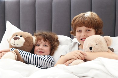 Photo of Cute little brothers with toys laying in bed at home