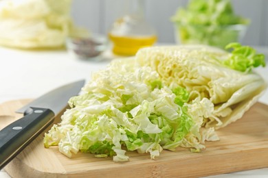 Photo of Cut Chinese cabbage and knife on white table, closeup