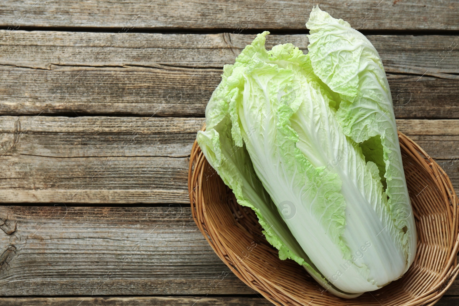 Fresh Chinese cabbage in wicker basket on wooden table, top view. Space for text Photo of Fresh Chinese cabbage in wicker basket on wooden table, top view. Space for text